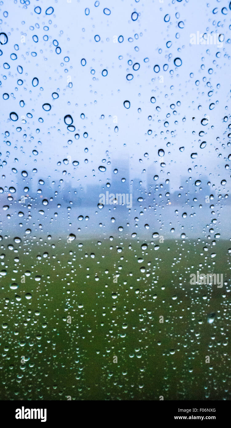 Droplets of rain on a window with the silhouette of a city in the background. Stock Photo
