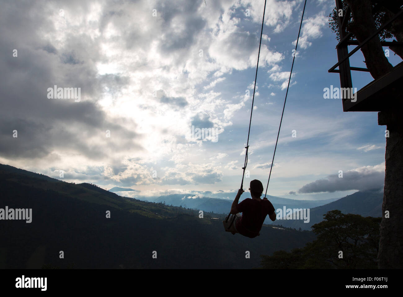 Silhouette of happy young man on a swing with a fantastic mountain view at the Casa del Arbol, Ecuador Stock Photo