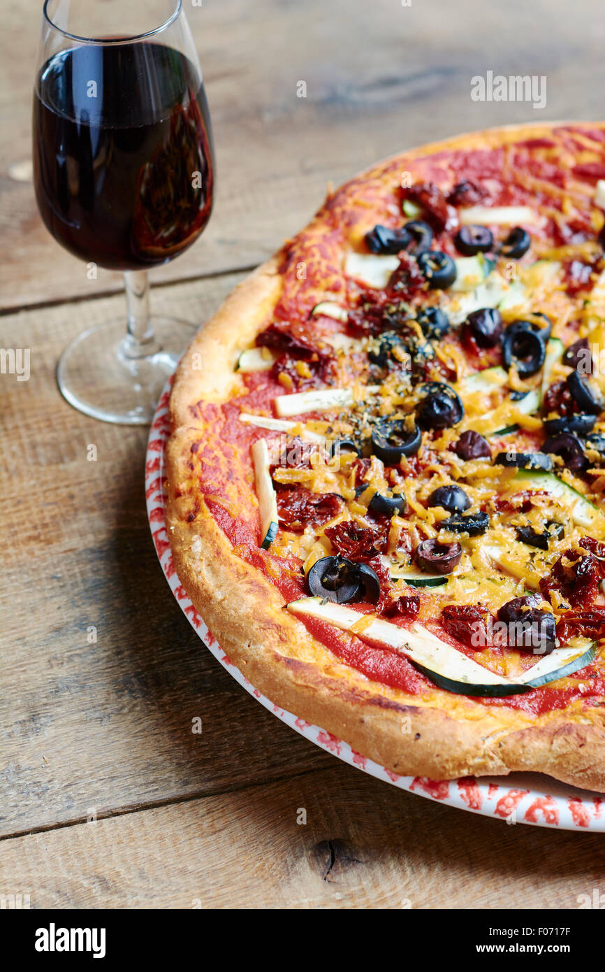 Homemade zucchini, sun-dried tomato and black olive pizza with a glass of red wine. Stock Photo
