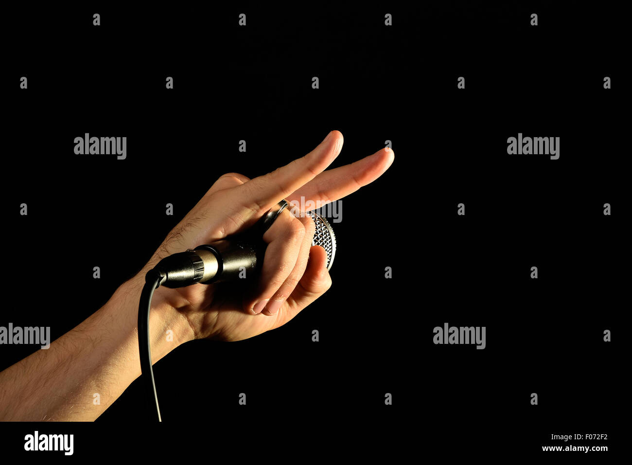 Male hand holding microphone with devil horns rock metal sign isolated on black background Stock Photo