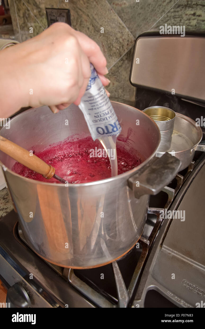 Pouring liquid fruit pectin into boiling blackberries and sugar mixture in the kitchen in Issaquah, Washington, USA Stock Photo