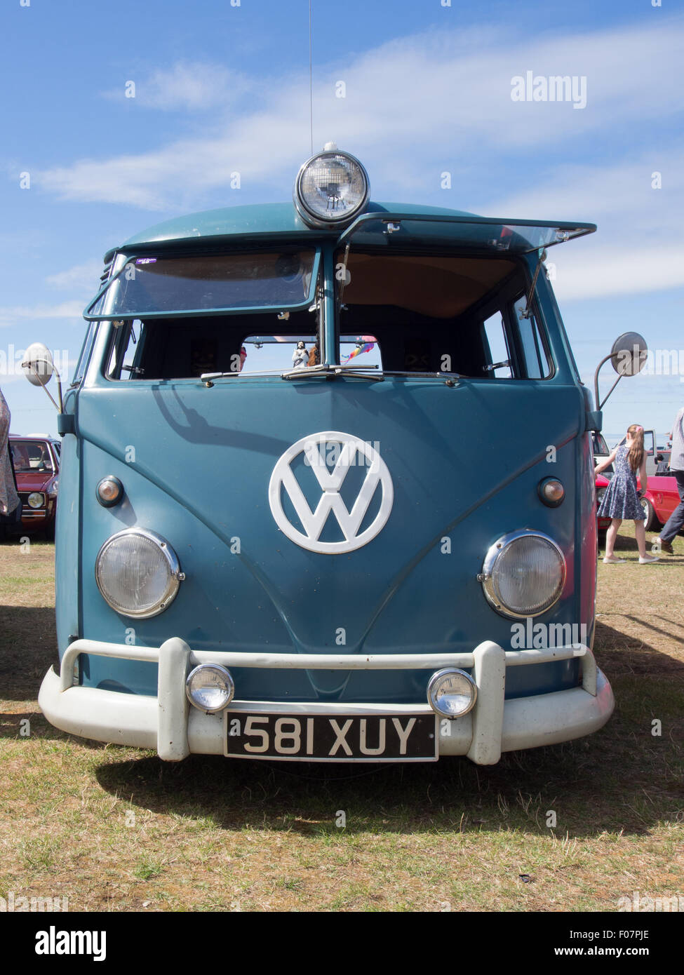 A VW split screen camper van with front windows open and VW sign on the front. Stock Photo