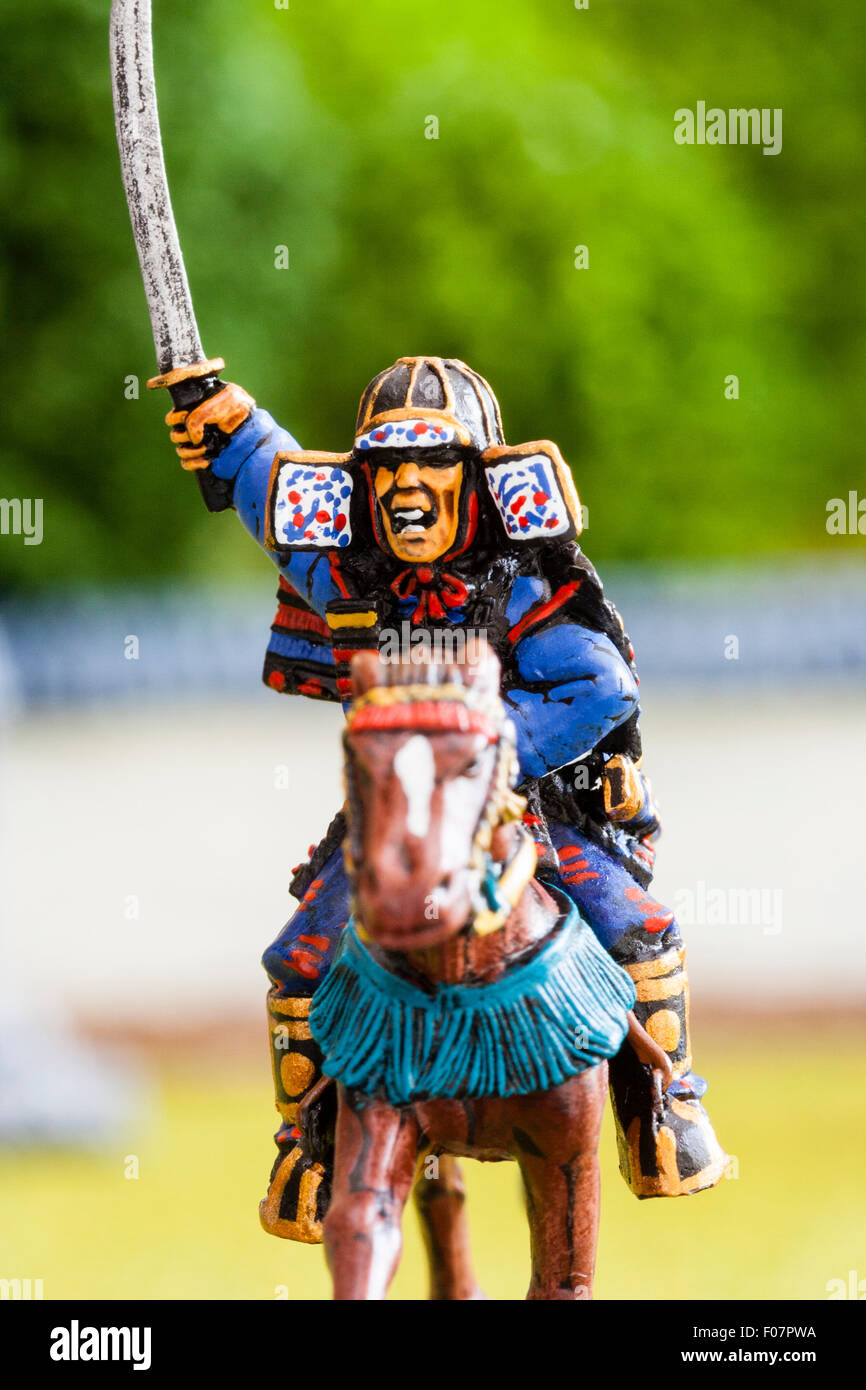 Close-up of metal painted scale model figures. Mounted Japanese samurai warrior holding sword, charging into battle. Table top war gaming. Stock Photo