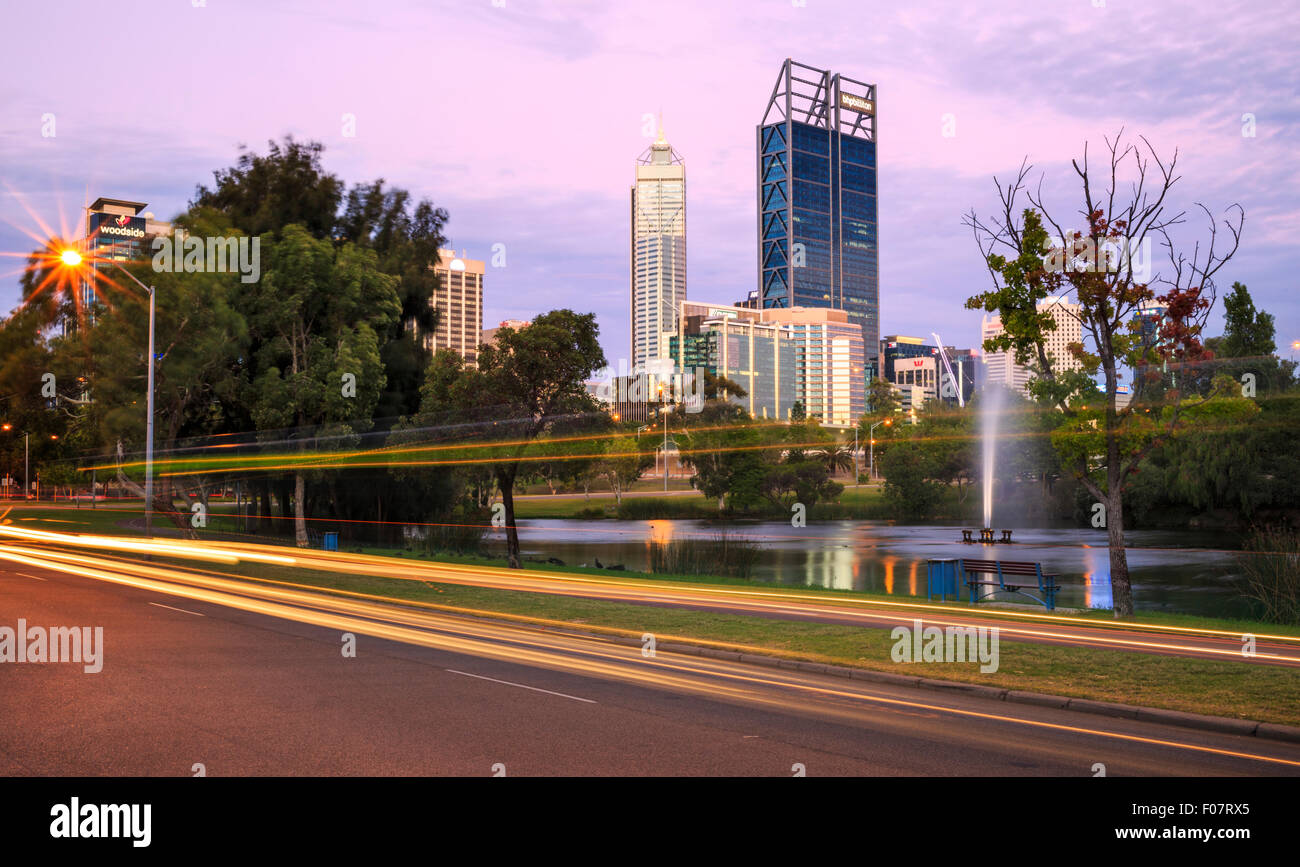 Car headlights streaking along the road at sunset with Perth city in