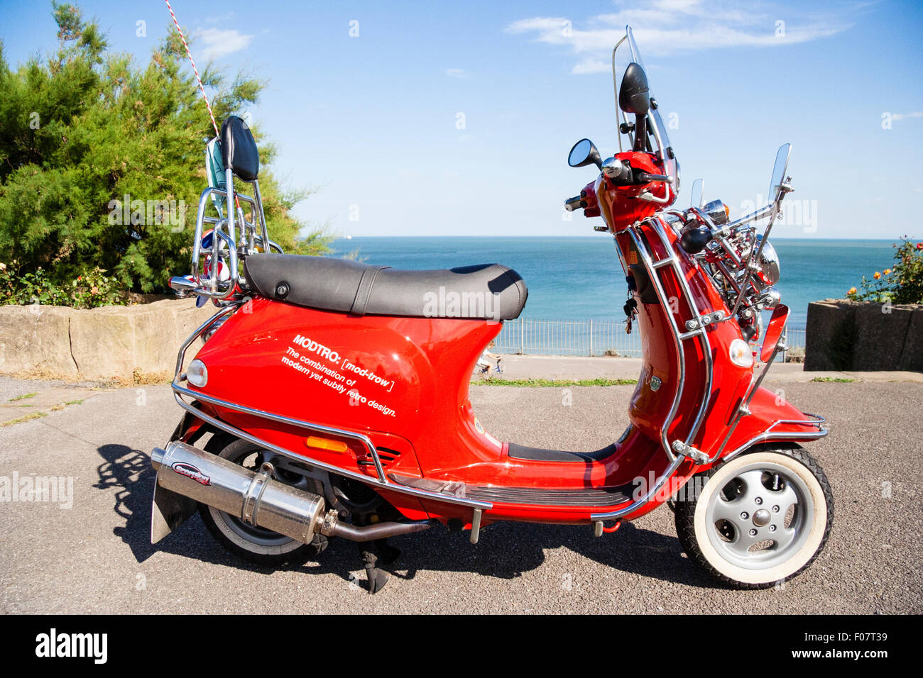 Motor Scooter, Italian Red Vespa ET4 125, modified, many wing mirrors as per Mods fashion cult look. Side view on seafront road, sea and sky behind. Stock Photo