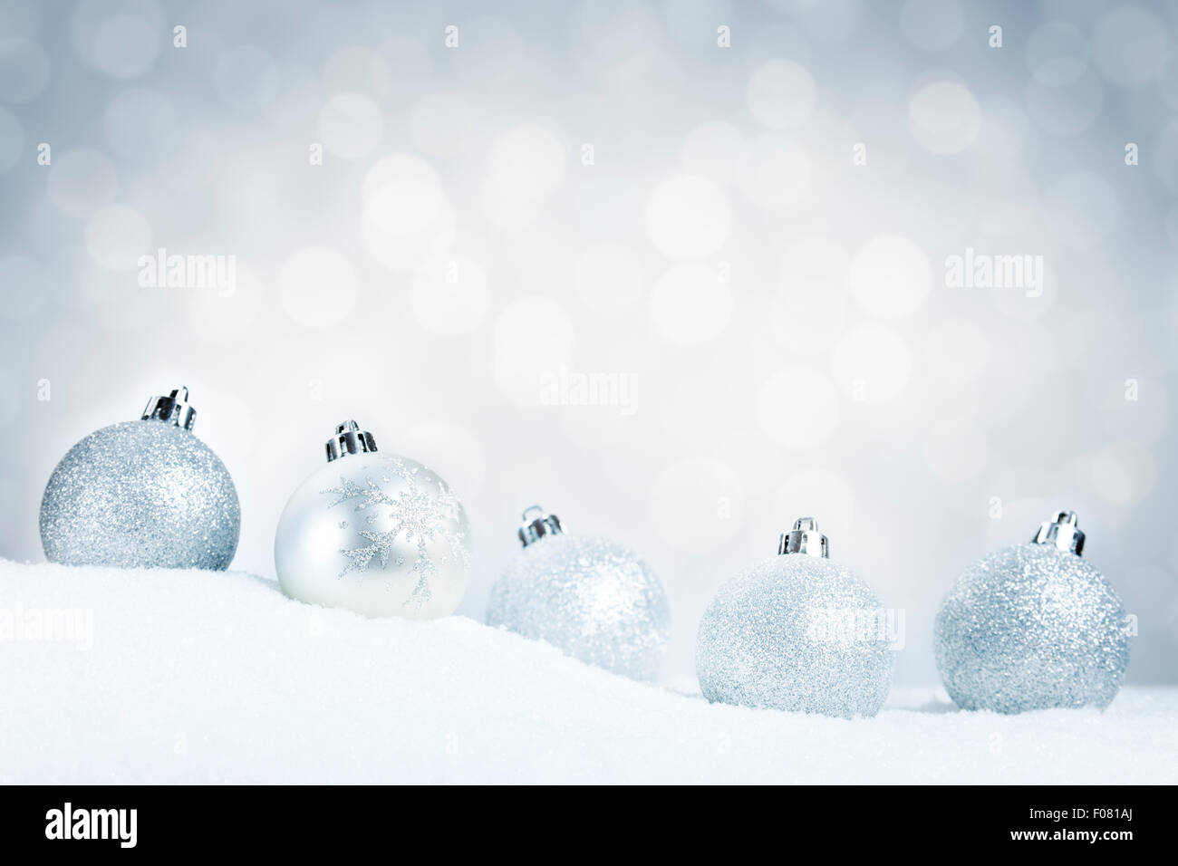 A row of silver Christmas baubles on snow with defocused silver and ...