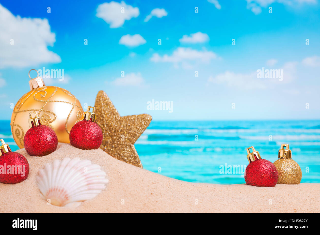 Christmas decorations and baubles in the sand on a beach on a bright and sunny day. Stock Photo