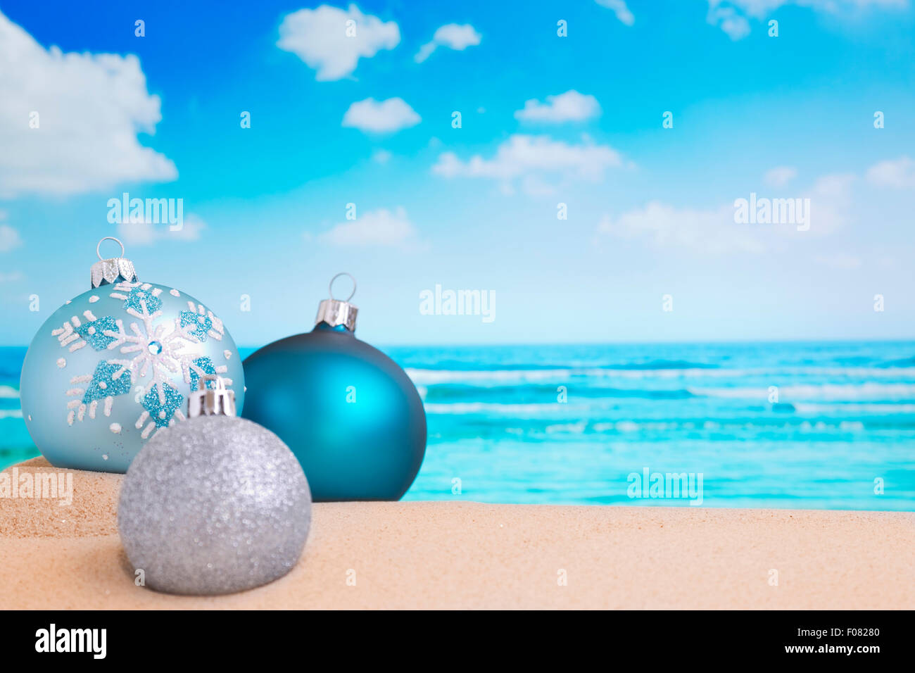 Christmas baubles in the sand on a beach on a bright and sunny day. Stock Photo