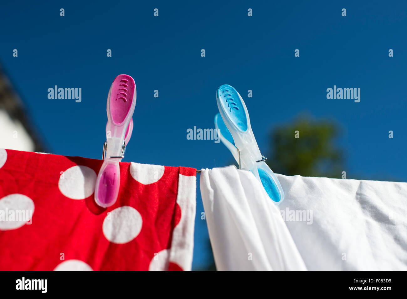 Red and white laundry drying in the sun pegged on washing line with coloured pegs. Stock Photo