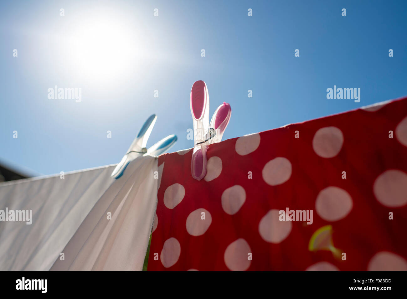 Red and white laundry drying in the sun pegged on washing line with coloured pegs. Stock Photo