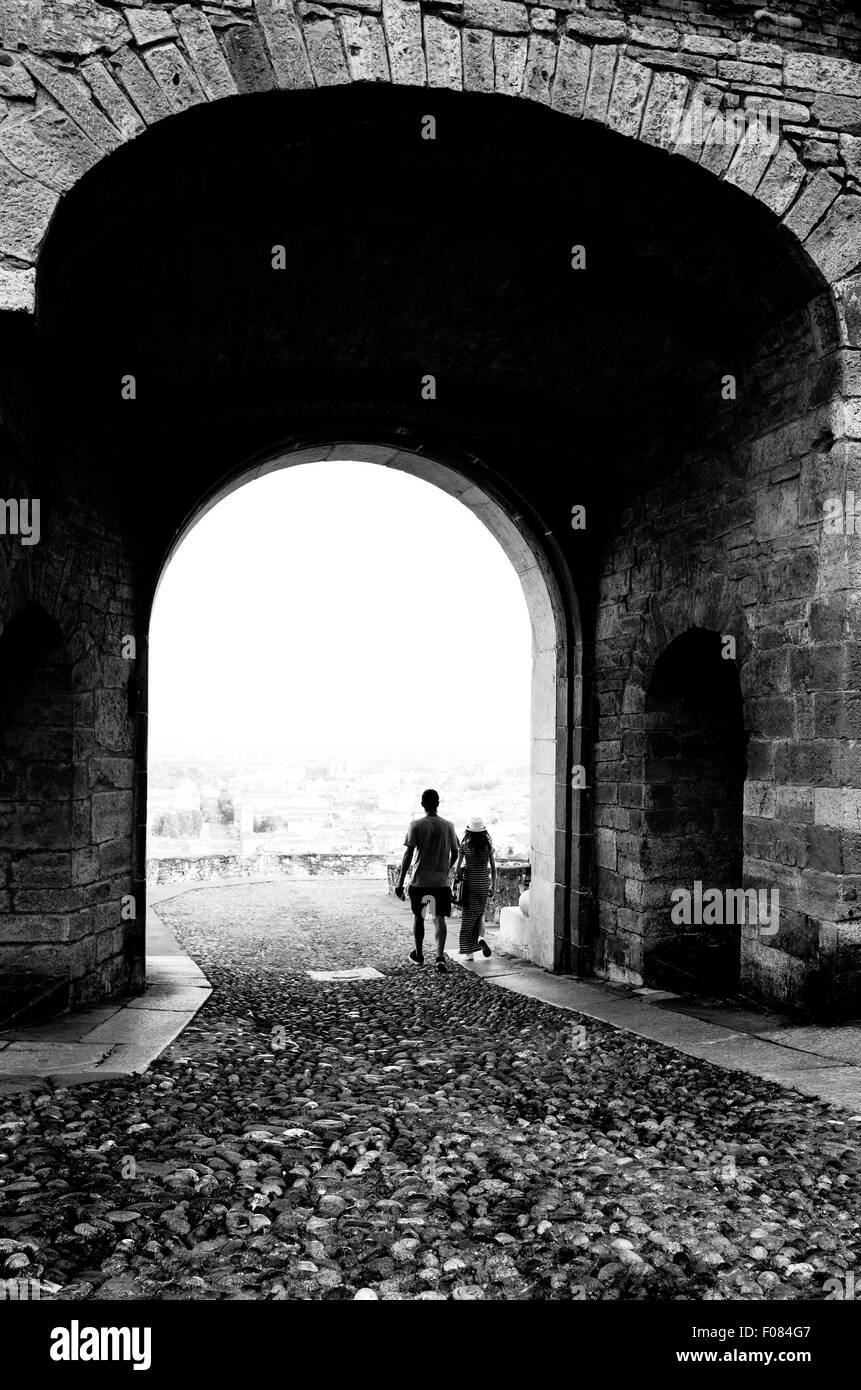 A young couple exiting from the antique arch door delitiming Bergamo Alta, Italy Stock Photo