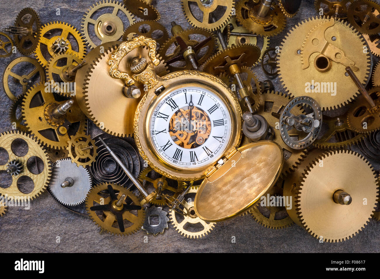 Pocket watch and a selection of dusty old brass clock parts. Stock Photo