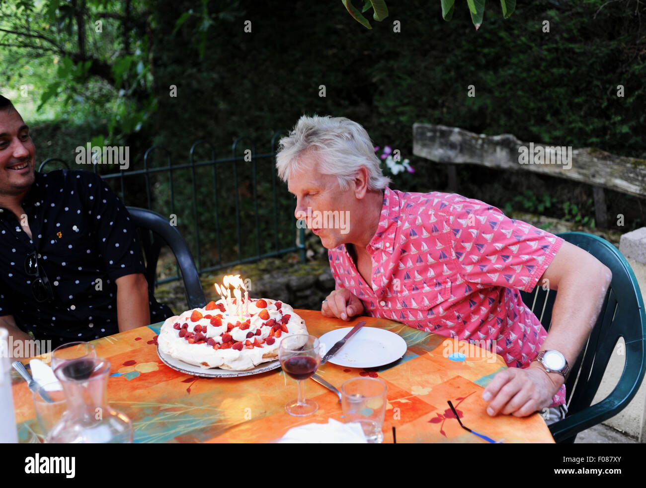 Man in his 50s celebrating his birthday blowing out candles on a cake Stock Photo
