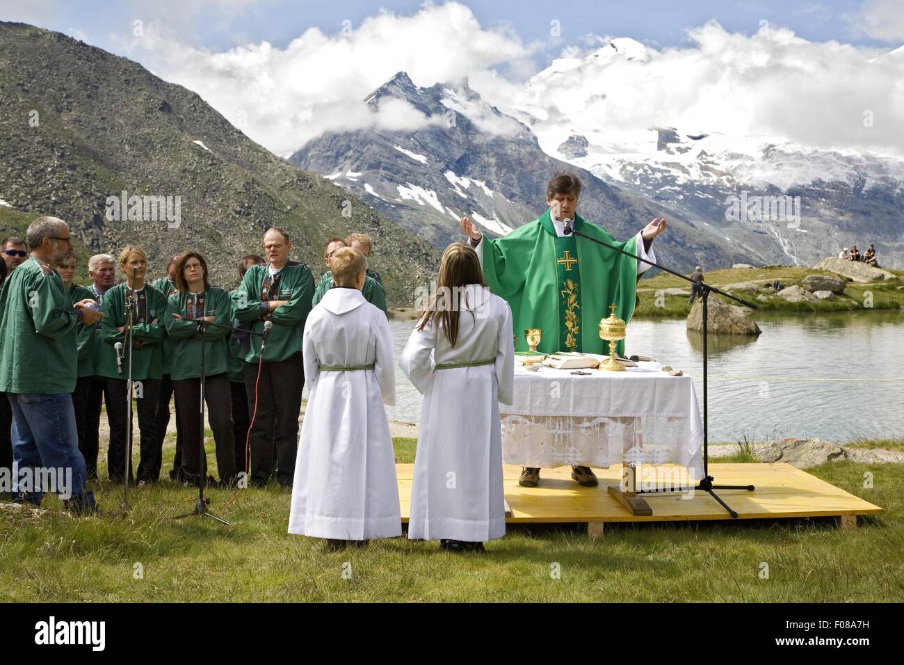 People standing around priest around at lake shore, mountain in background Stock Photo