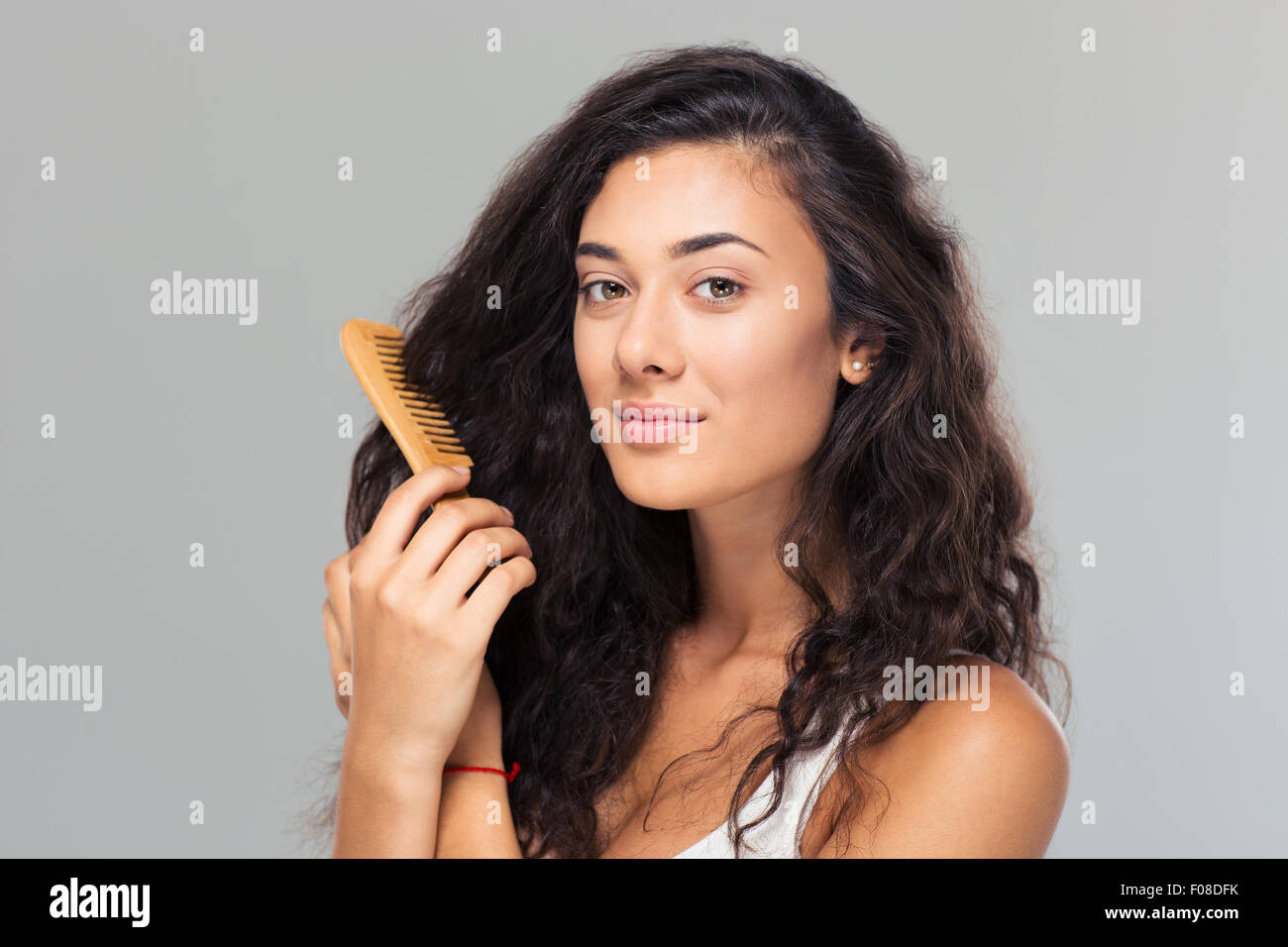 Happy cute woman combing her hair over gray background. Looking at camera Stock Photo