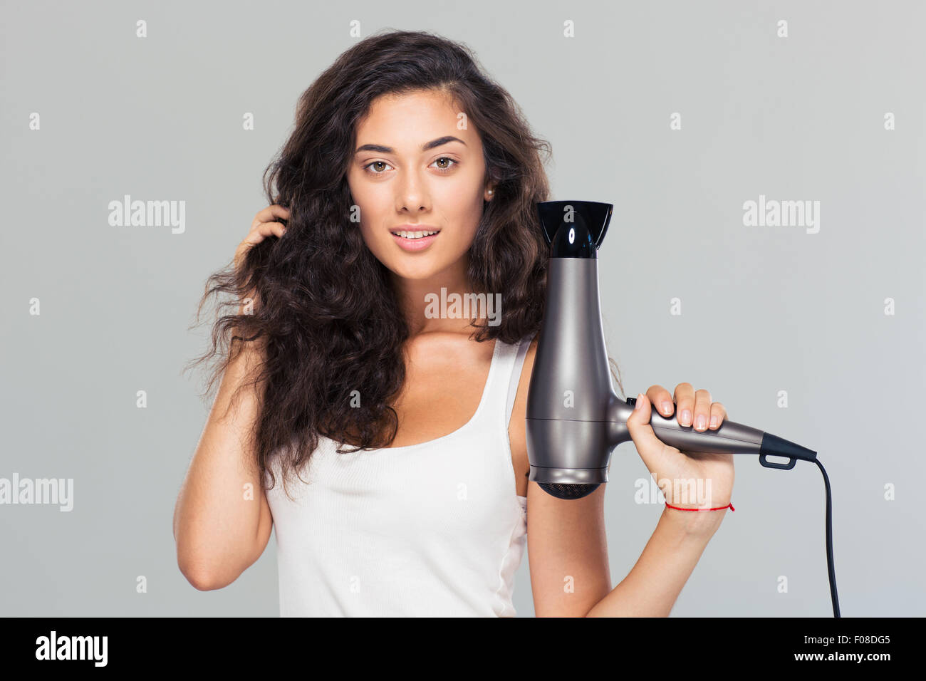 Happy beautiful woman holding hairdryer over gray background. Looking at camera Stock Photo