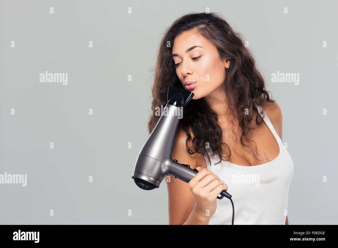 Portrait of a young pretty woman blowing on hairdryer over gray background Stock Photo