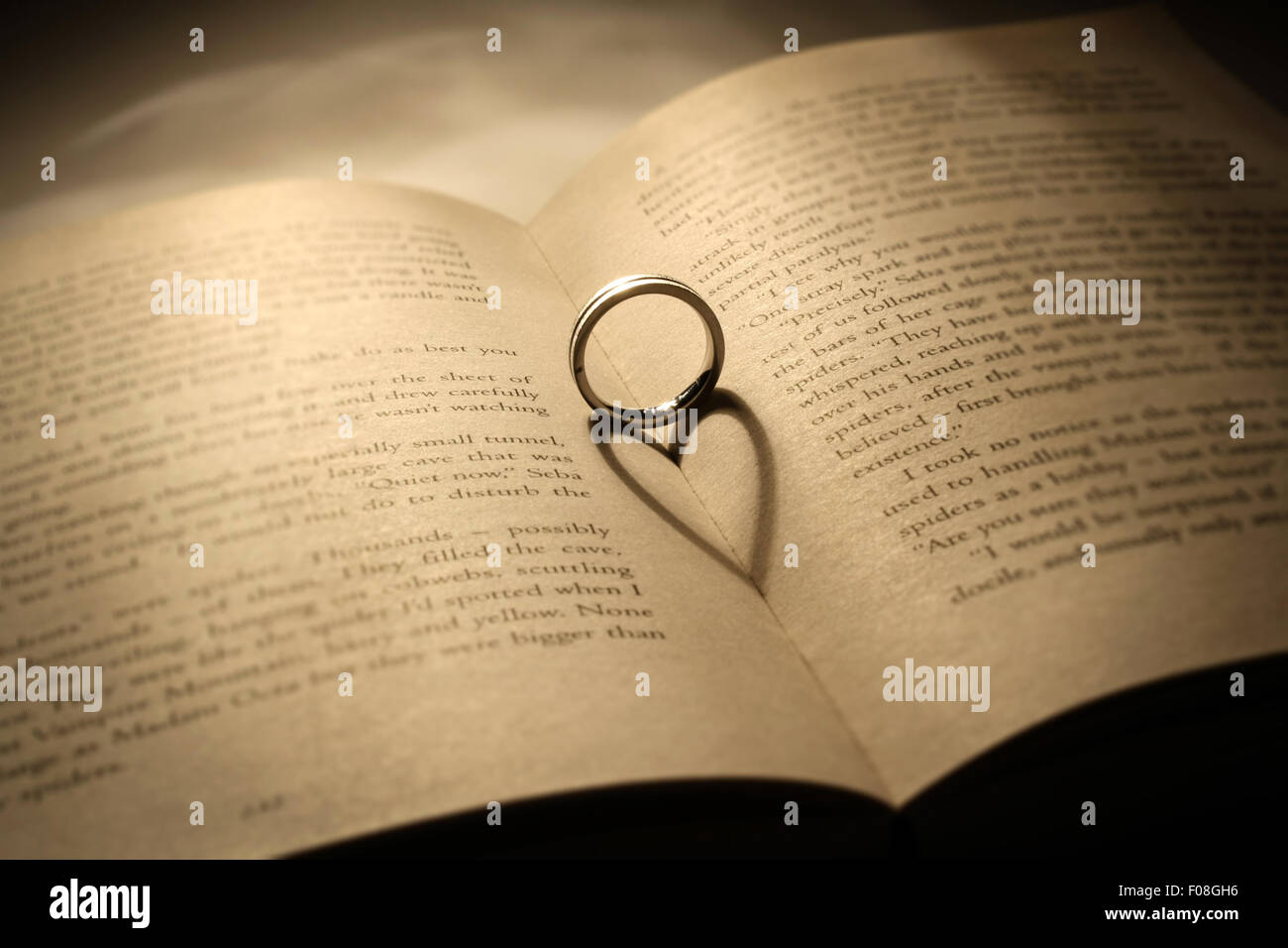 A silver ring casts a heart shaped shadow on an opened book Stock Photo
