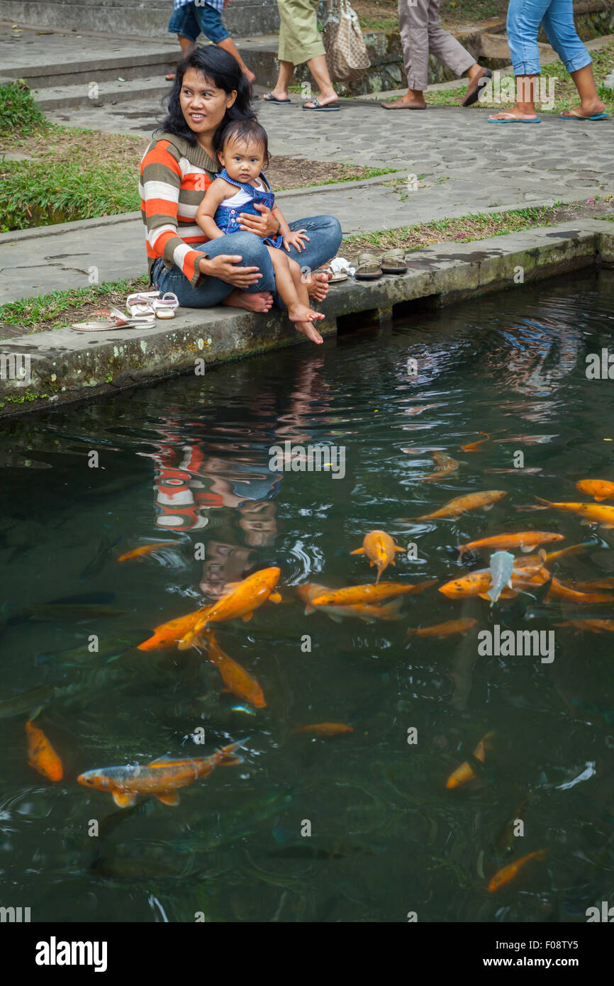 Woman with a lap child seeing goldfishes at a pond in Tirta Gangga, Karangasem, Bali, Indonesia. Stock Photo