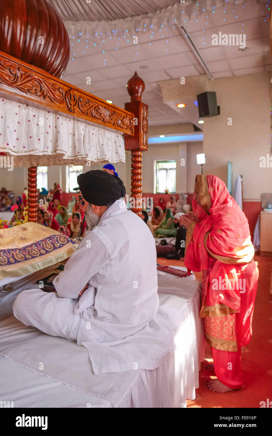 Priest sitting at Vigil and Woman Worshiper at Brent Cross Sikh Temple Stock Photo