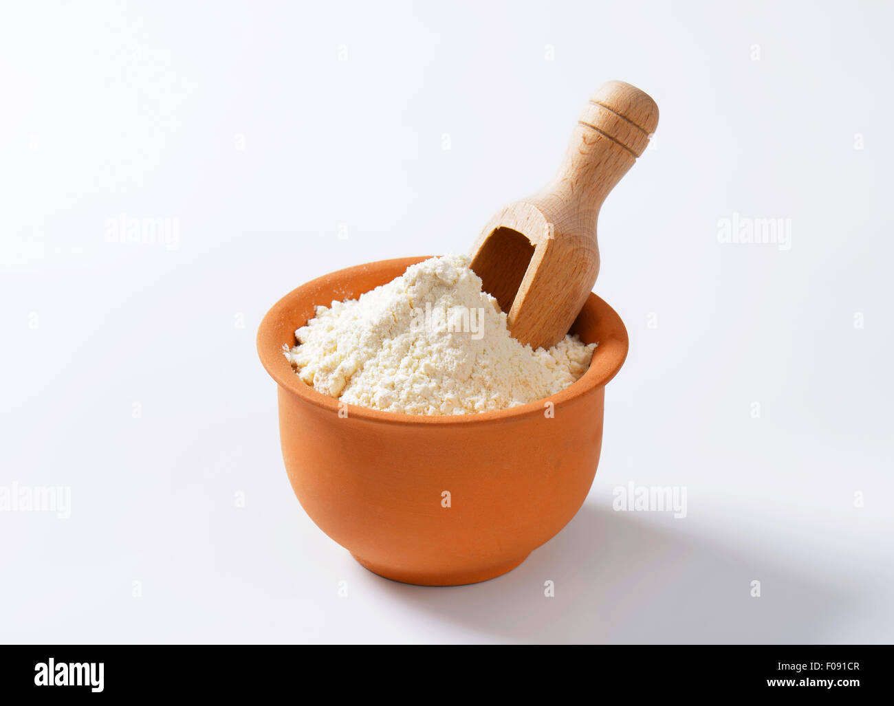 Finely ground flour and wooden scoop in terracotta bowl Stock Photo