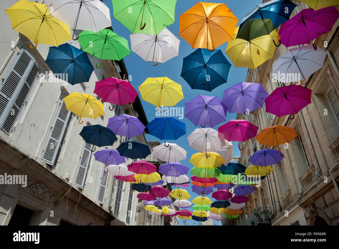 Brightly coloured floating umbrellas fill the sky above Rue Jean Jaures, Arles,Bouches-du-Rhône department, Provence, France Stock Photo
