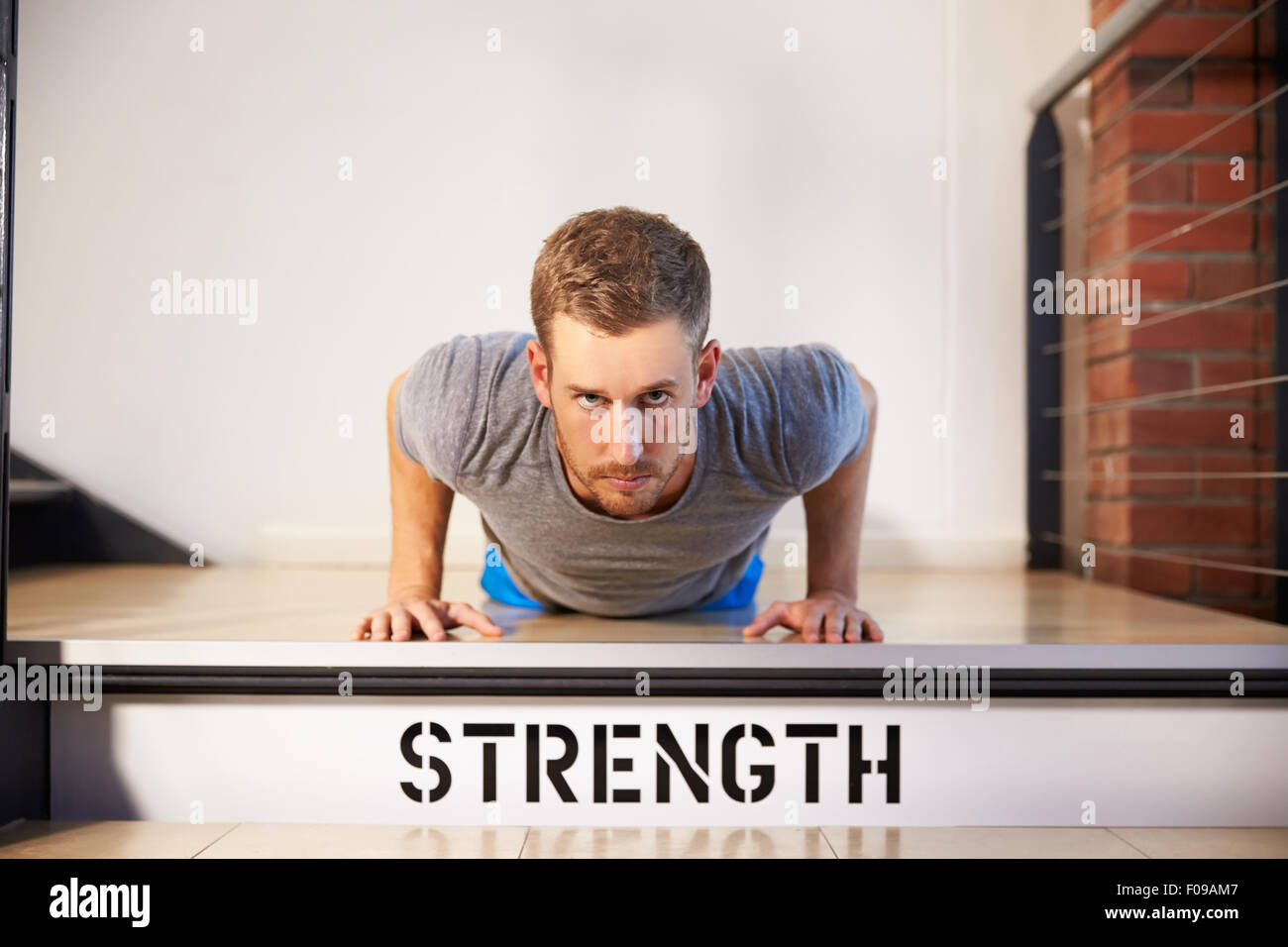 Man In Gym Doing Press-Ups On Step Labeled Strength Stock Photo