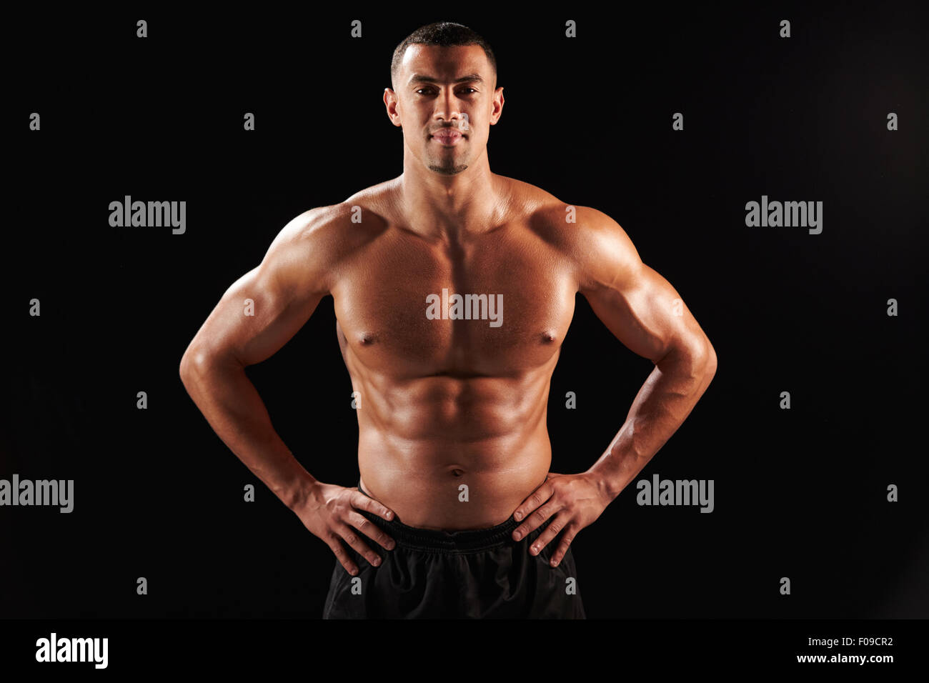 Smiling bare chested male body builder with hands on hips Stock Photo