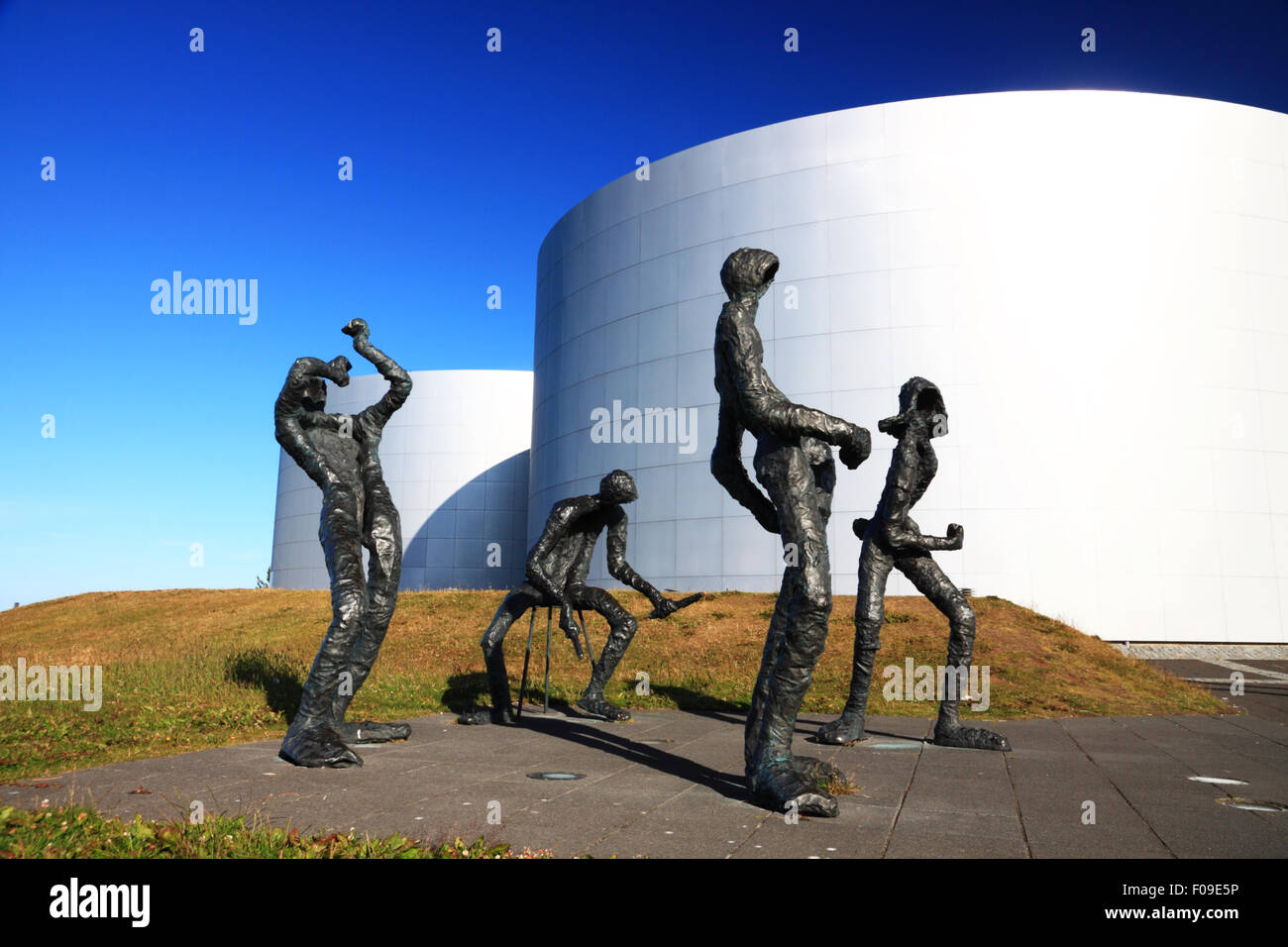 A group of bronze figures depicting musicians beside a group of metal storage tanks. Stock Photo