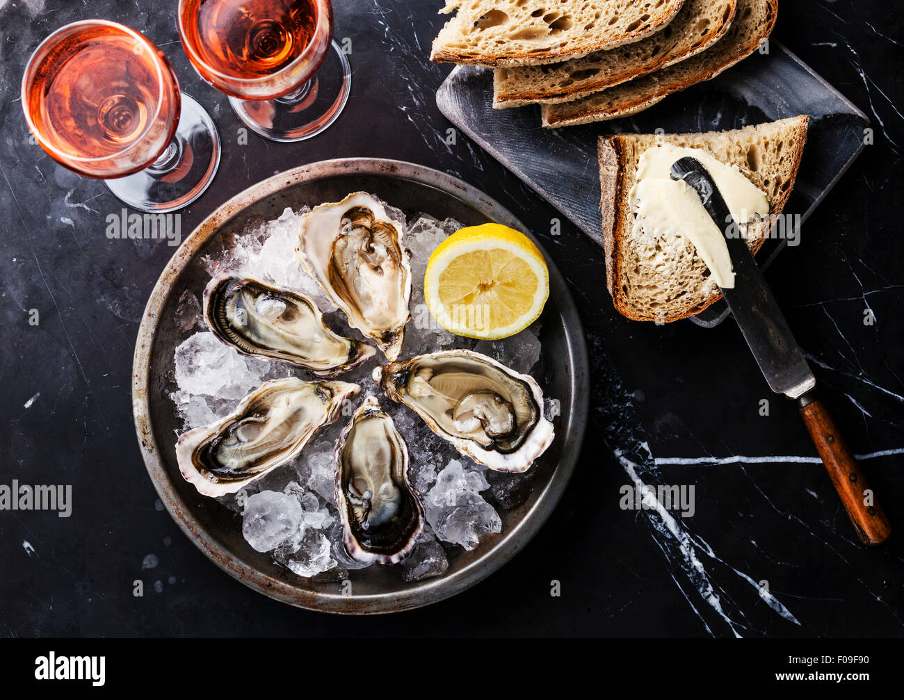 Opened Oysters on metal plate, bread with butter and rose wine on dark marble background Stock Photo