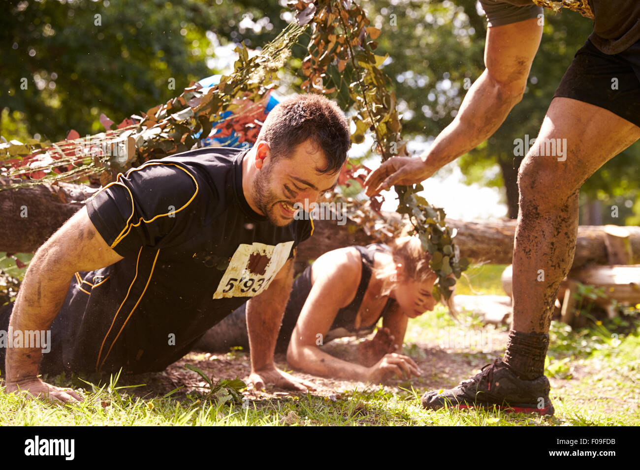 Assault course competitor helping others crawl under nets Stock Photo