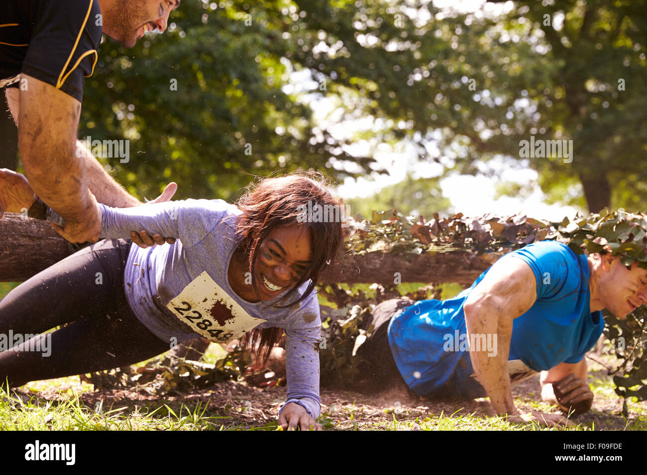 Assault course competitor helping others crawl under nets Stock Photo