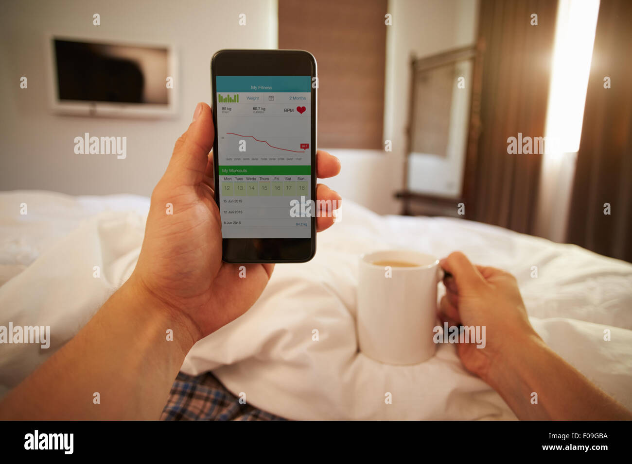 Man In Bed Looking At Health Monitoring App On Mobile Phone Stock Photo