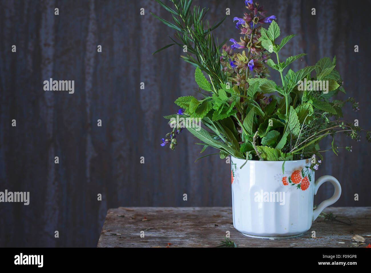 Old cup with assortment of fresh herbs mint, oregano, thym, blooming sage over old wooden background. Natural day light. Stock Photo