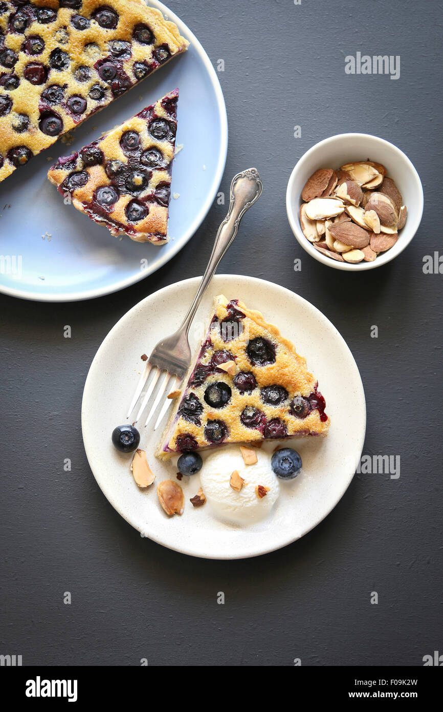 A slice of blueberry tart on a plate with ice cream and roasted almonds Stock Photo