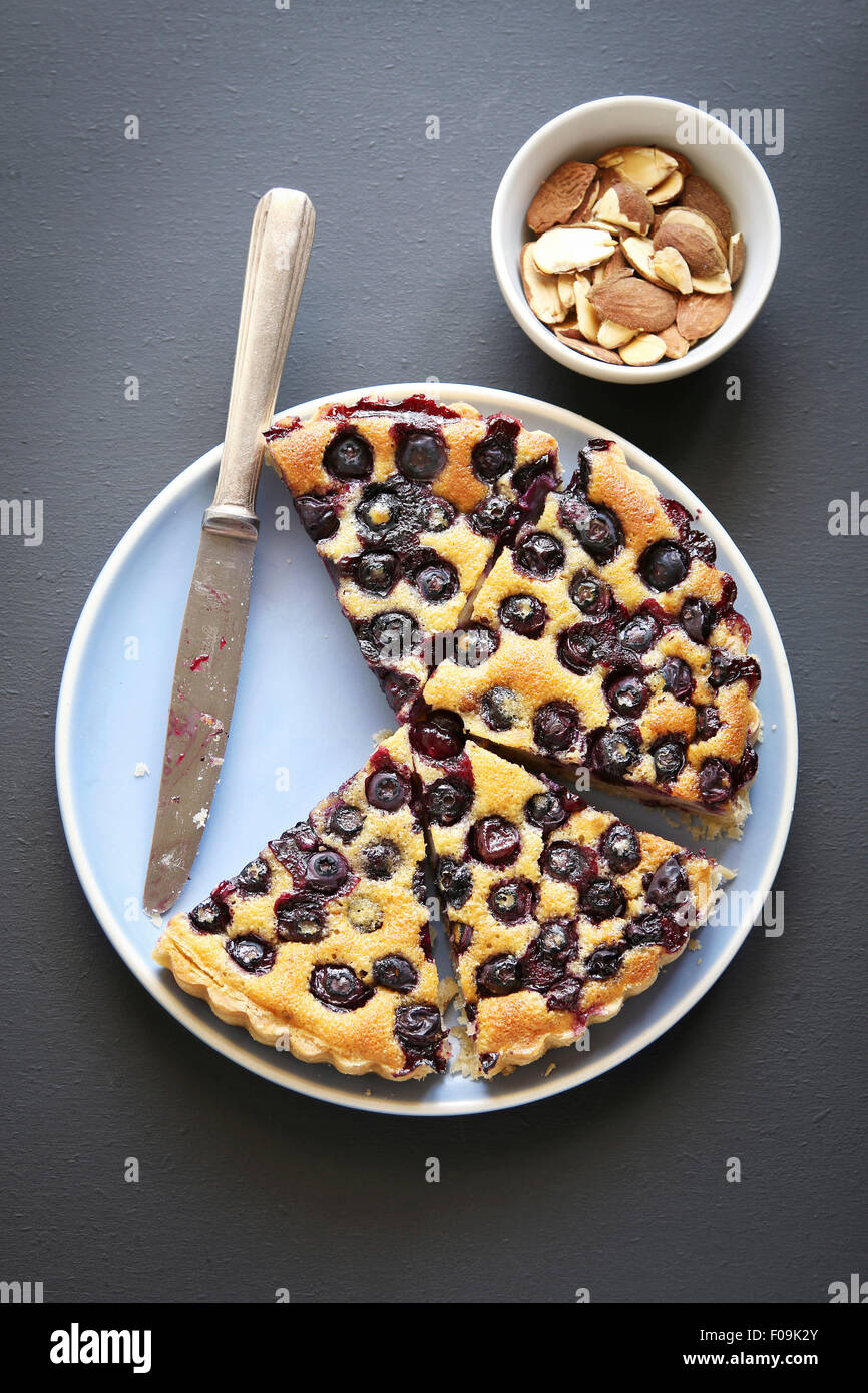 Slices of blueberry tart on a blue plate and roasted almonds.Top view Stock Photo