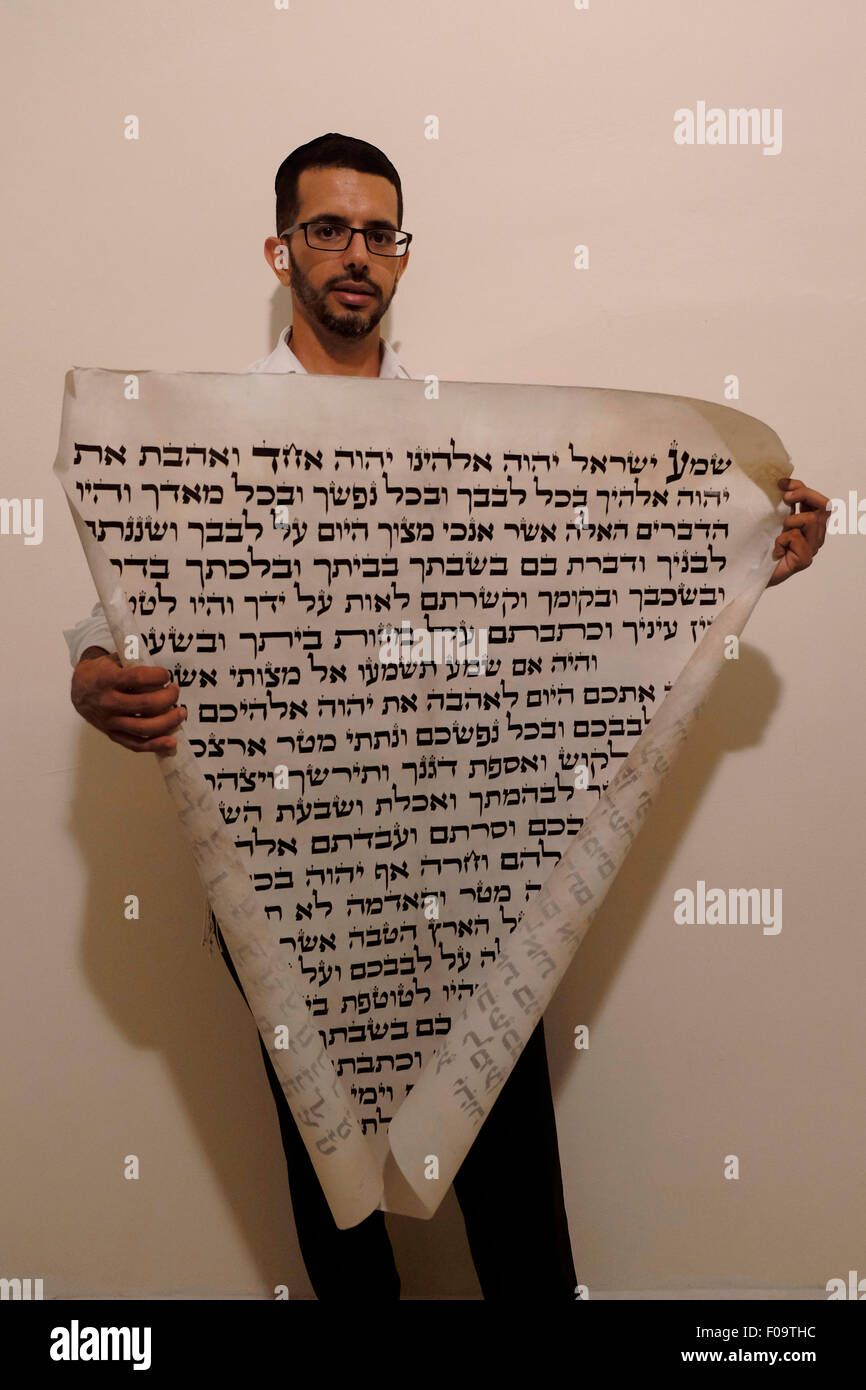 A religious Jewish man holds a parchment of a huge Mezuzah inscribed