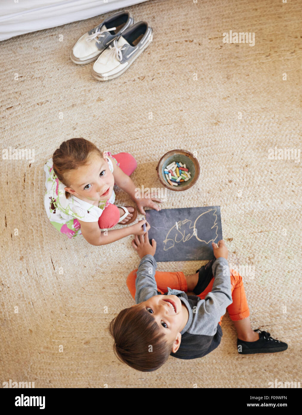 Top view of two little kids sitting on floor looking up at camera while drawing. Stock Photo