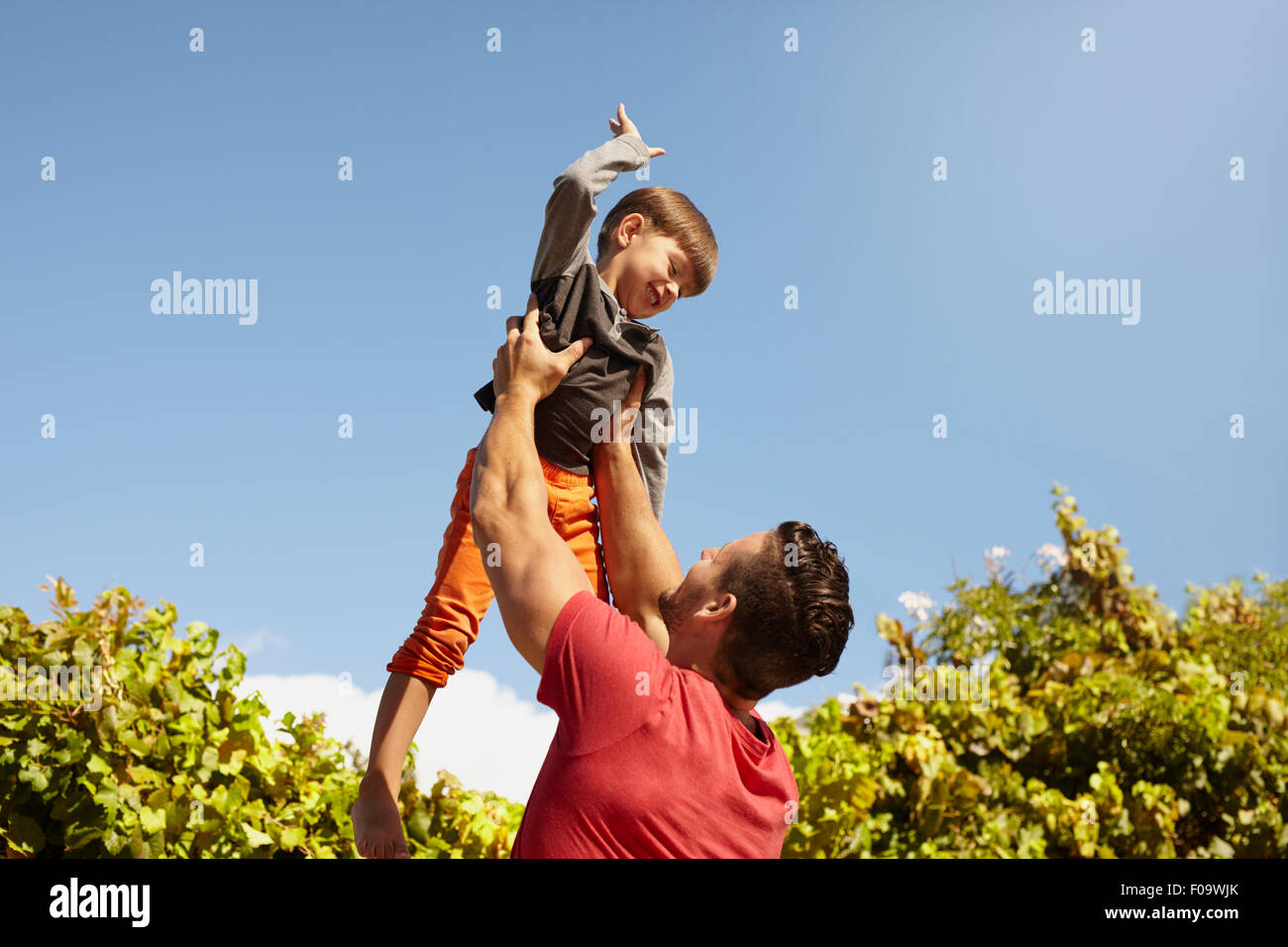 Shot of young man holding his little son high up in air against sky on a sunny day. Happy father and son having fun outdoors Stock Photo