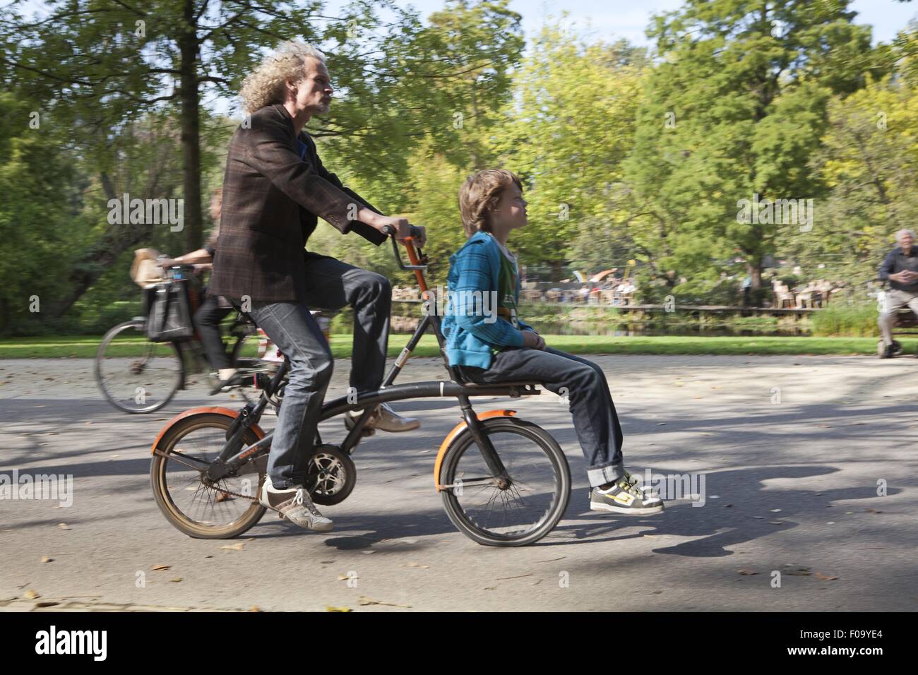 Man riding bicycle while boy sitting on porter in Vondelpark, Amsterdam, Netherlands Stock Photo