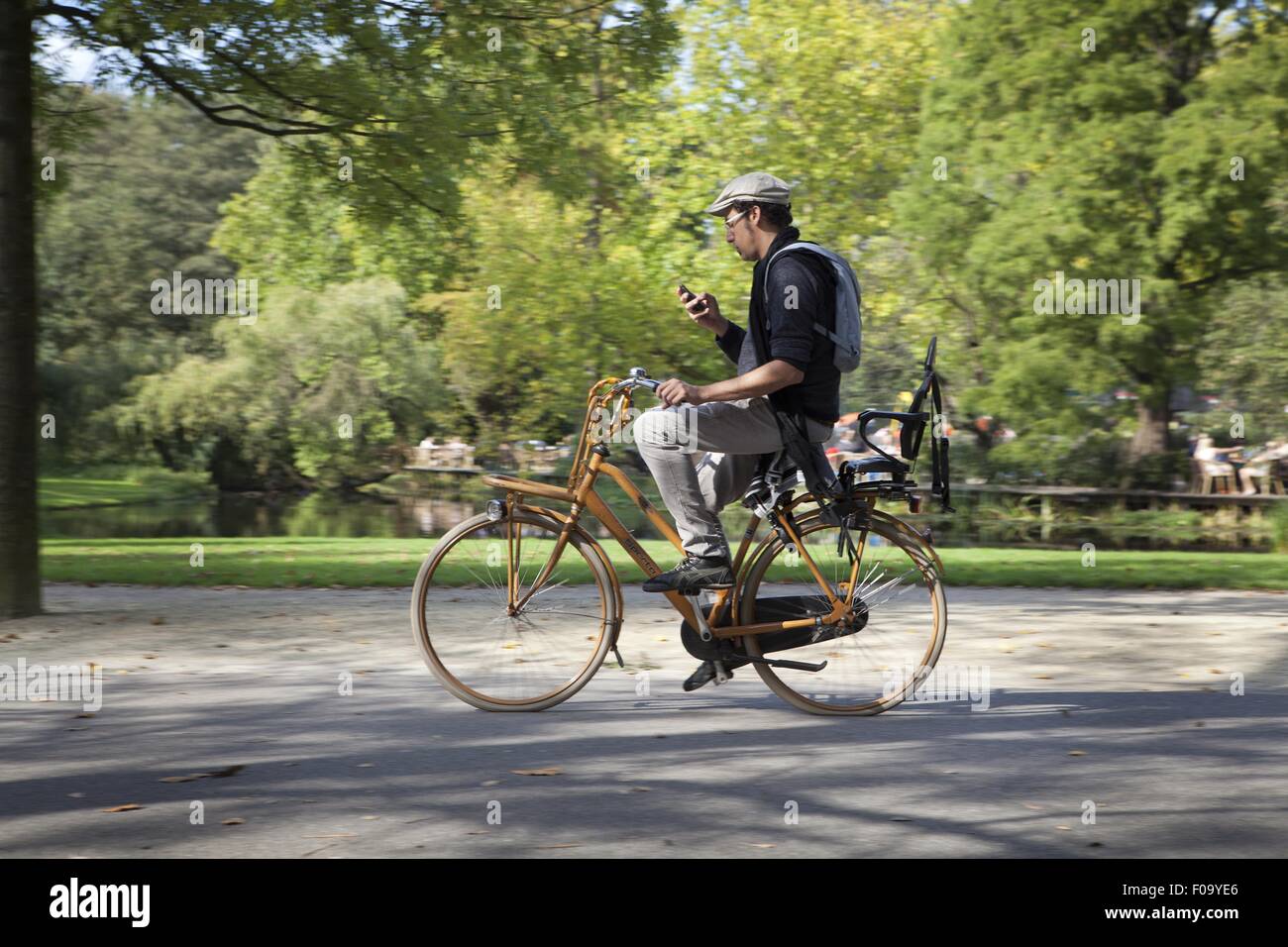 Man riding bicycle and checking mobile in Vondelpark, Amsterdam, Netherlands Stock Photo