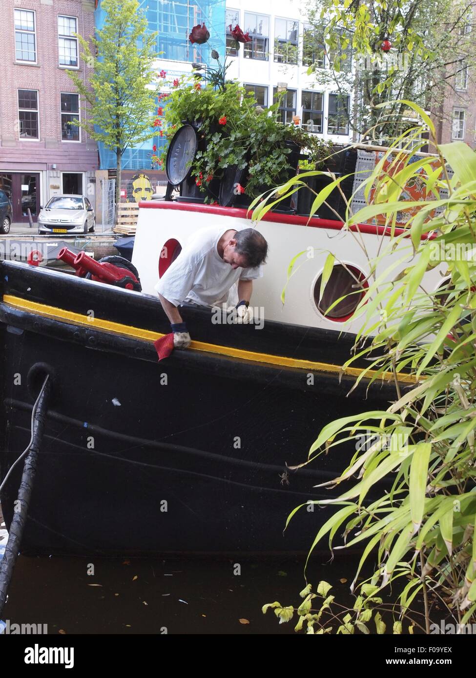 Man cleaning houseboat in Prinsengracht canal, Amsterdam, Netherlands