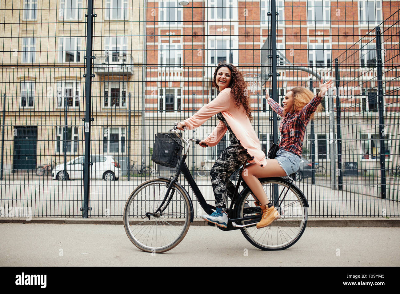 Portrait of two happy young women enjoying bike ride on city street. Female friends riding on one bicycle. Stock Photo