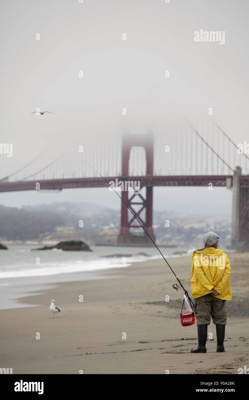 Man on beach fishing in front of Golden Gate Bridge covered with fog, San Francisco, USA Stock Photo