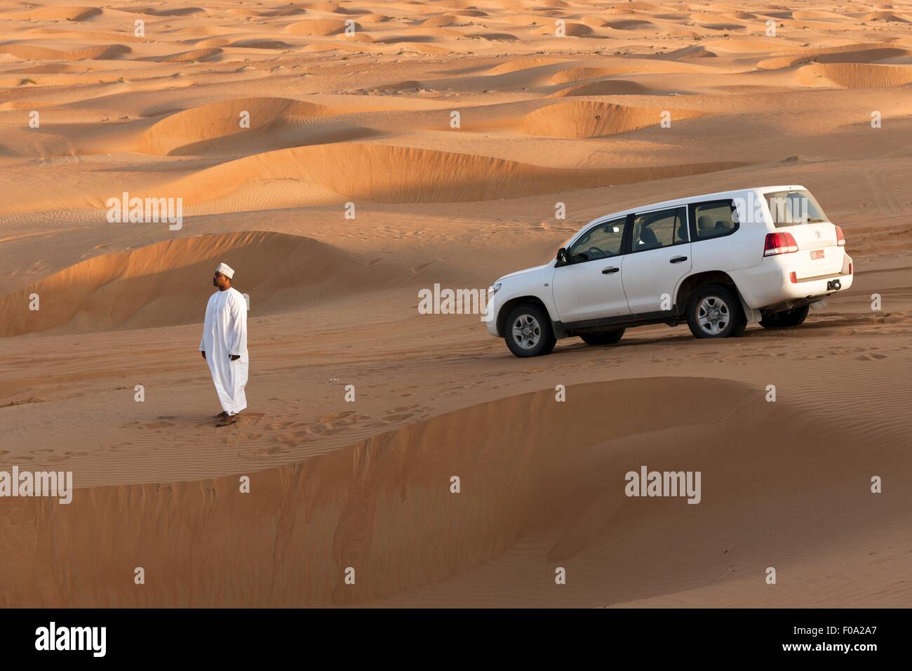 Man wearing white dishdasha standing in front of SUVs in Wahiba sands, Oman Stock Photo