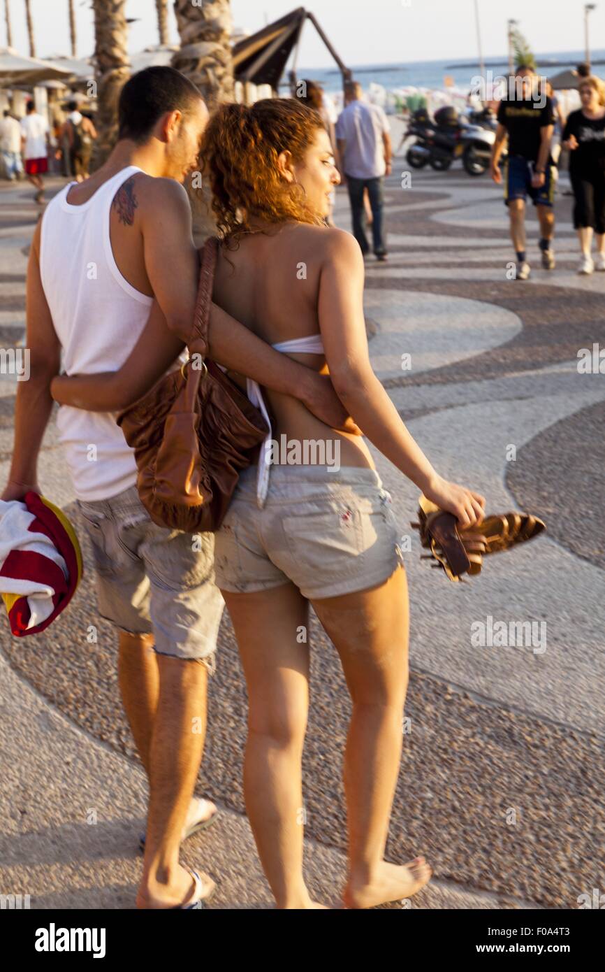 Rear view of couple walking with arms around on boardwalk, Tel Aviv, Israel Stock Photo