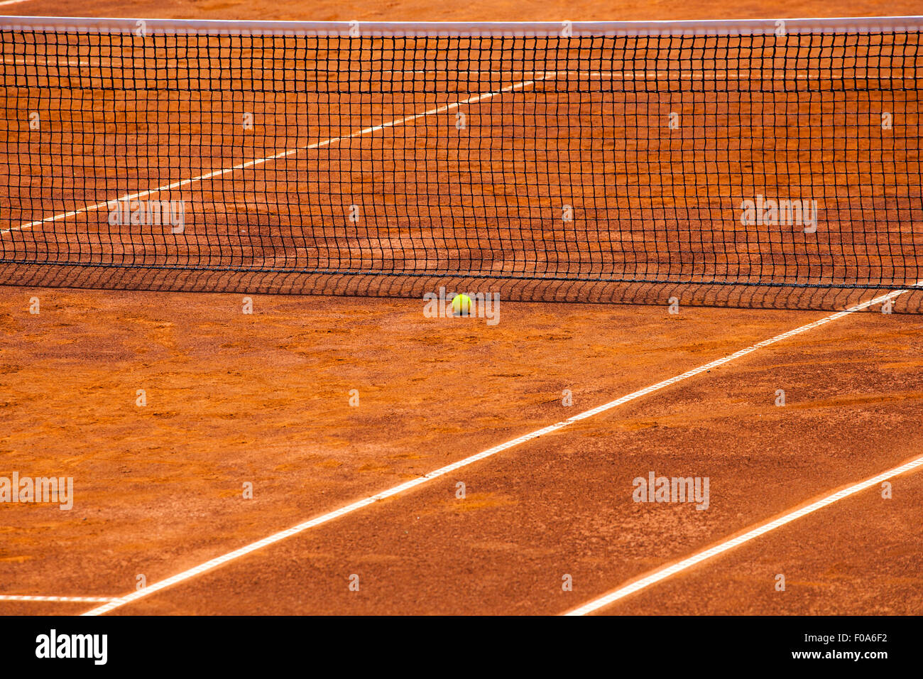 Stock image of an empty tennis court with net and yellow ball close to it. It is a clear sunny day and the court is ready before Stock Photo