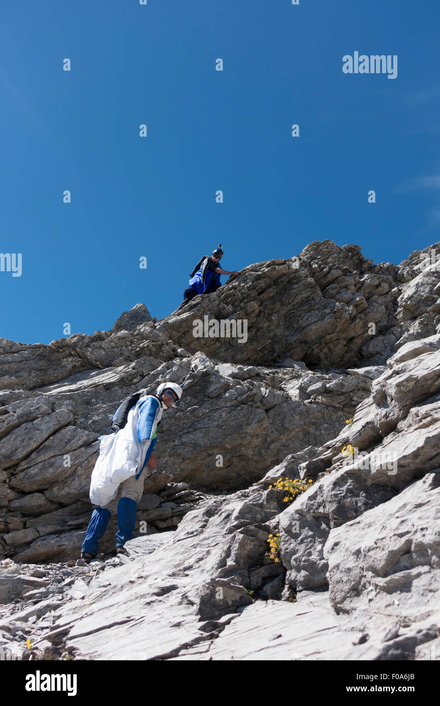 Wingsuit BASE jumpers are climbing down on a rope to the exit platform and prepare their wingsuit and jumps from the cliff. Stock Photo