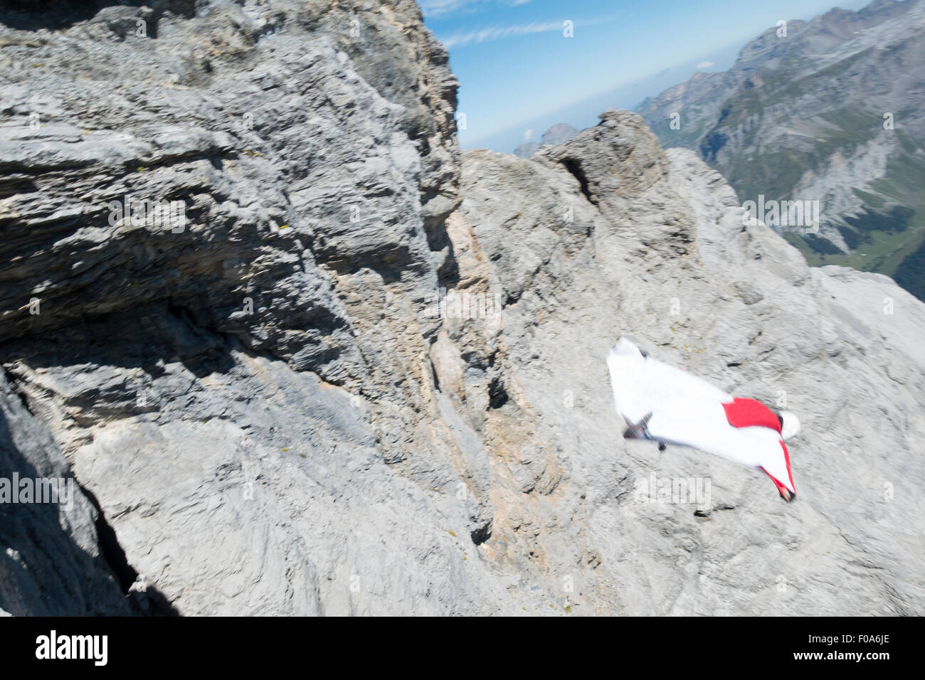 Wingsuit BASE jumper exited off a cliff downwards the valley and started flying with his birdman suit. Stock Photo