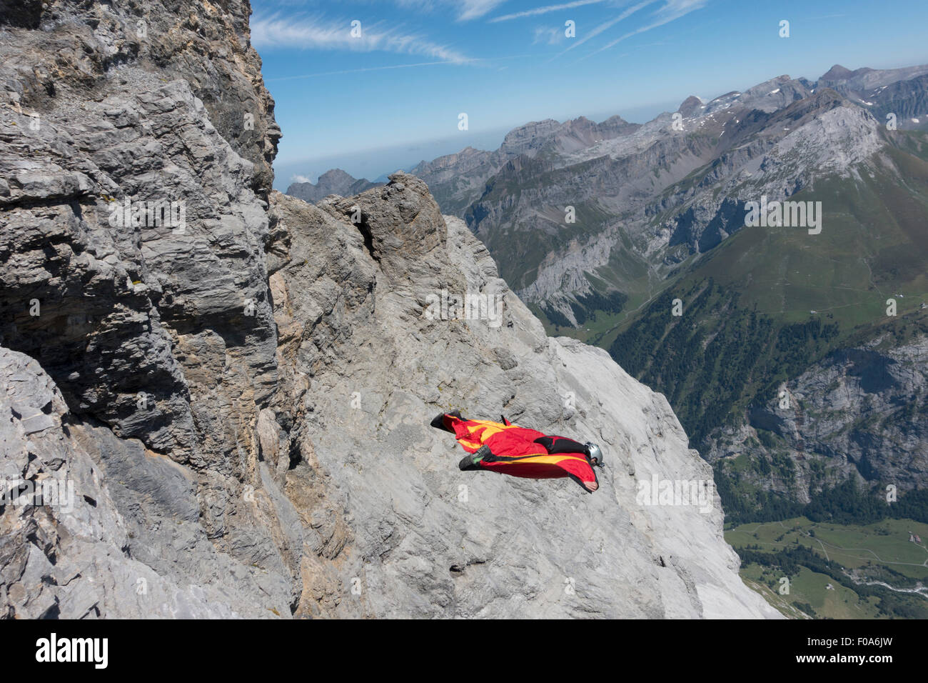 Wingsuit BASE jumper exited off a cliff downwards the valley and started flying with his birdman suit. Stock Photo